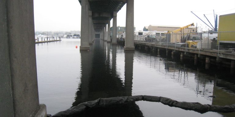 Image from the water looking down the length of the bridge with most bridge columns visible. Construction barge is in place on the right.